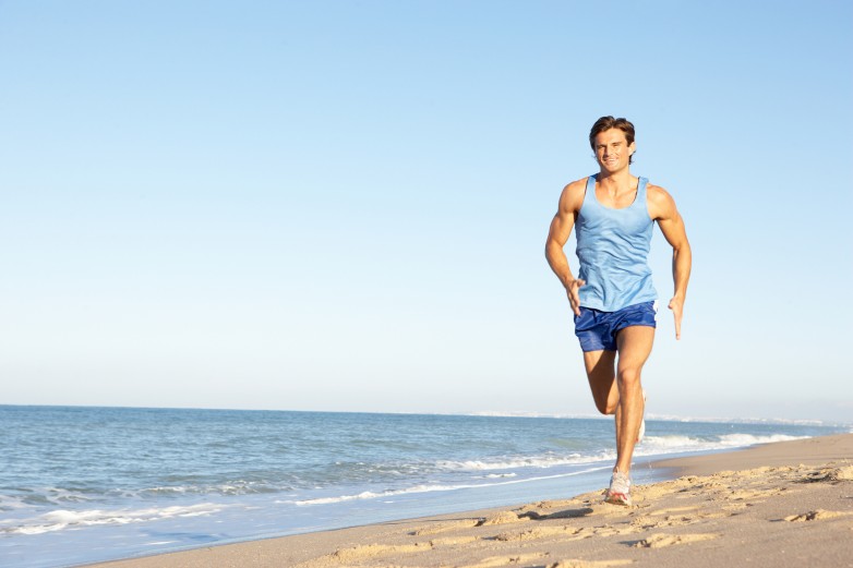 Young Man In Fitness Clothing Running Along Beach