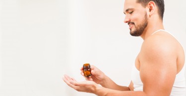 Profile view of a guy with a beard taking some pills from a bottle in front of a bathroom mirror